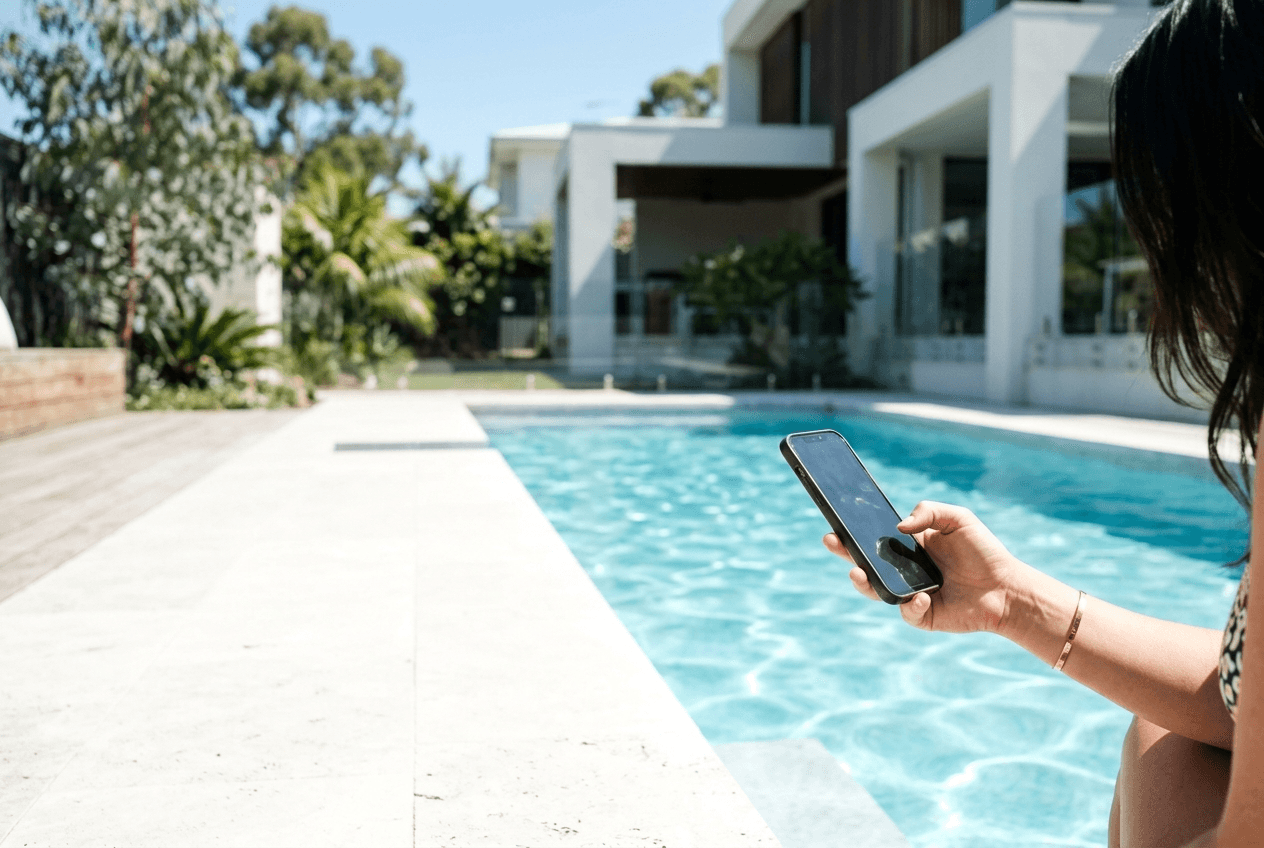 Woman browsing on her phone beside a modern Australian pool and contemporary home